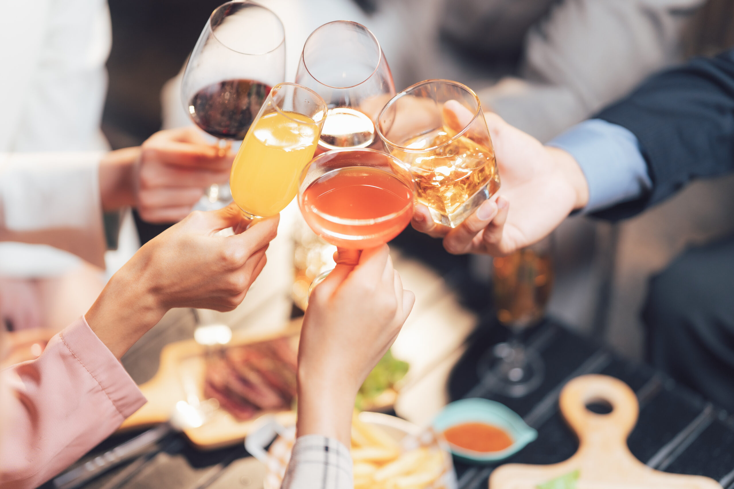 Cheers to Celebration: Close-up shot of diverse hands clinking glasses filled with various beverages, signifying friendship, celebration and togetherness during a social gathering.